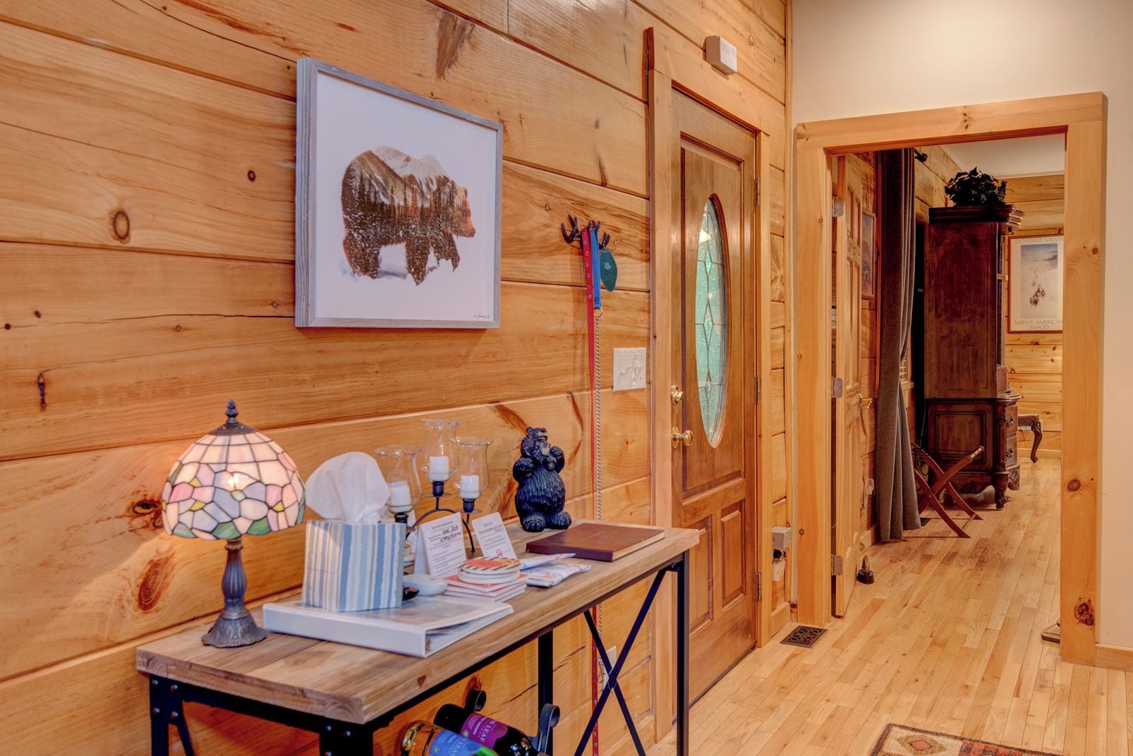 A wooden interior with a table displaying a bear painting, a stained glass lamp, and various items.