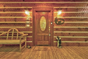 A wooden cabin entrance with a bench, a welcome mat, and a bear statue. - Hebron Falls Cabin (Boone)