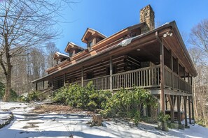 A log cabin with a wooden deck and multiple windows, surrounded by trees and snow. - Hebron Falls Cabin (Boone)