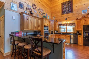 A wooden cabin-style kitchen with a central island, bar stools, and various kitchen appliances.