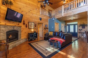 A spacious living room with a stone fireplace, a leather sofa, and a television mounted on the wall. - Porridge Pot (Marion)