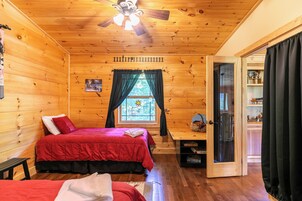 A cabin room with two beds, a ceiling fan, a window with curtains, and a door leading to another room.