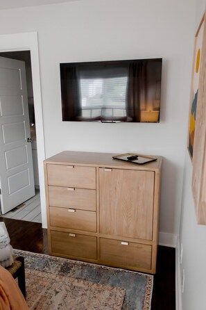 A room with a wooden cabinet, a television mounted on the wall, and a patterned rug on the floor.