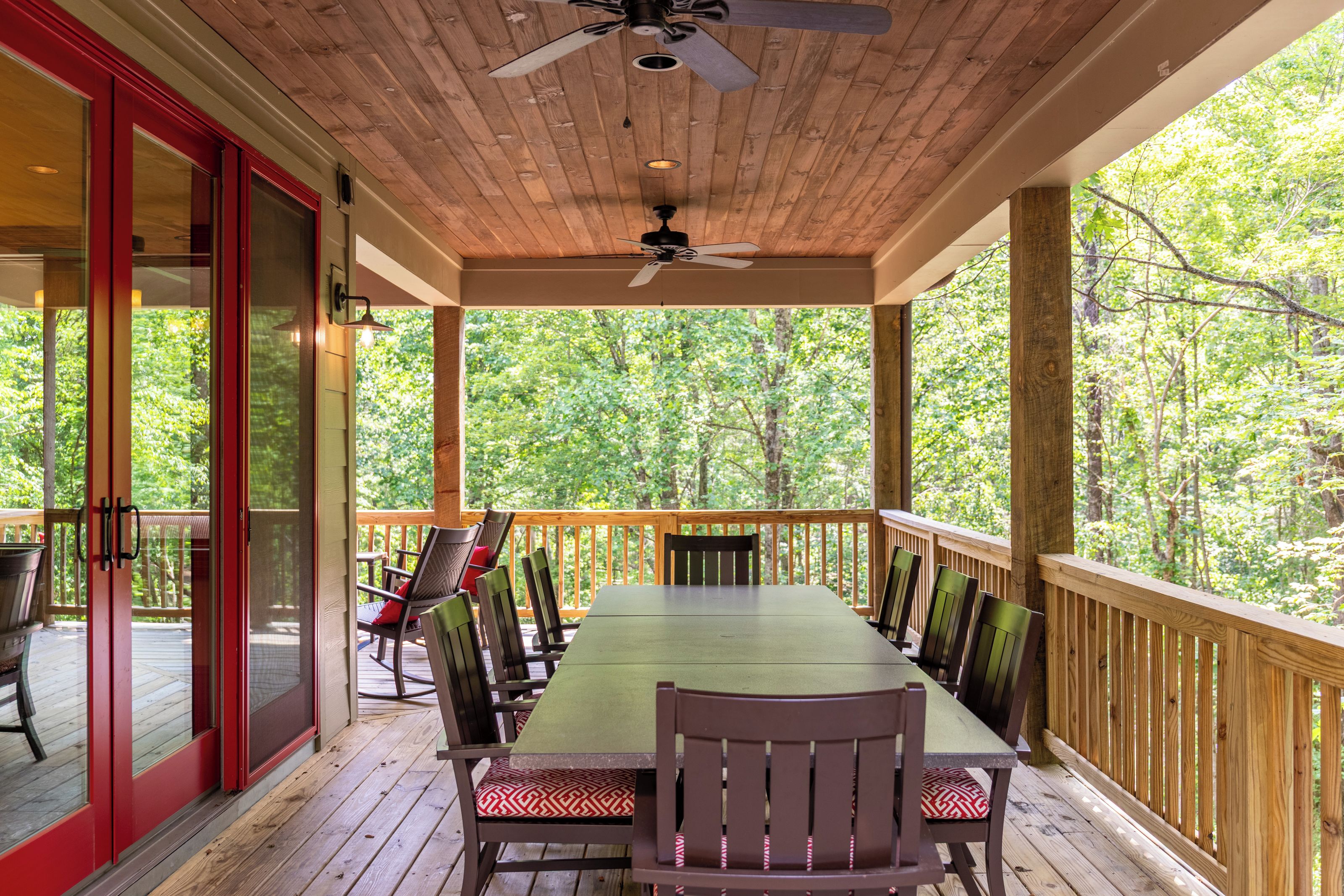 Un espacio de comedor al aire libre cubierto con una mesa, sillas, ventilador de techo y vista a un bosque.
