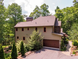 A two-story house with a garage, surrounded by trees and a landscaped garden. - Fern Ridge Lodge at Sweetgrass (Blowing Rock)