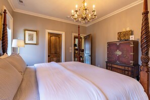 A bedroom with a large bed, a wooden wardrobe, a chandelier, and a door leading to another room. - Fern Ridge Lodge at Sweetgrass (Blowing Rock)