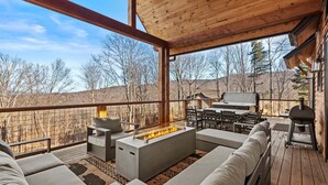Eine überdachte Terrasse im Freien mit Feuerstelle, Sitzgelegenheit und Grill.