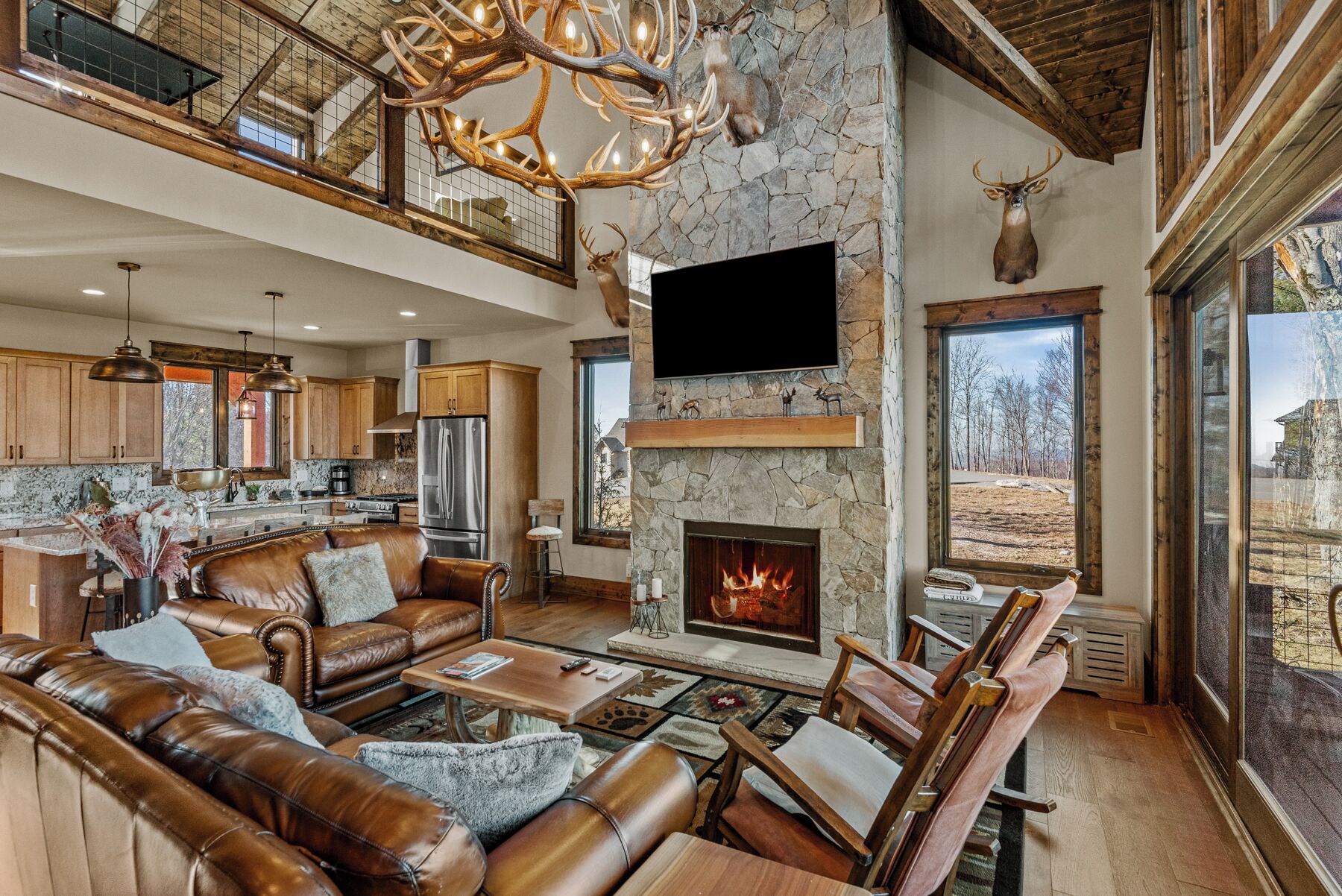 A spacious living area with a stone fireplace, leather furniture, and a large TV mounted on the wall.