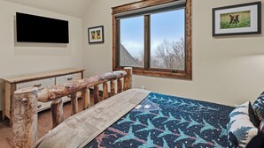 Ein Schlafzimmer mit einem Holzbett, einem Schreibtisch, einem großen Fenster und gerahmten Bildern an der Wand.