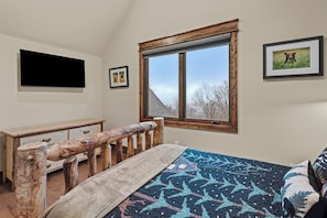 Ein Schlafzimmer mit einem Holzbett, einem Schreibtisch, einem großen Fenster und gerahmten Bildern an der Wand.