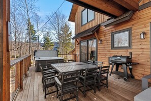 A wooden deck with a table and chairs, a barbecue grill, and a hot tub. - Haven at Eagles Nest (Banner Elk)