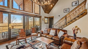 Ein geräumiges Wohnzimmer mit hohen Decken, großen Fenstern, einem Ledersofa und einer Treppe mit Holzwertungen.