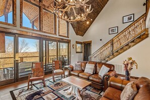 Ein geräumiges Wohnzimmer mit hohen Decken, großen Fenstern, einem Ledersofa und einer Treppe mit Holzwertungen.