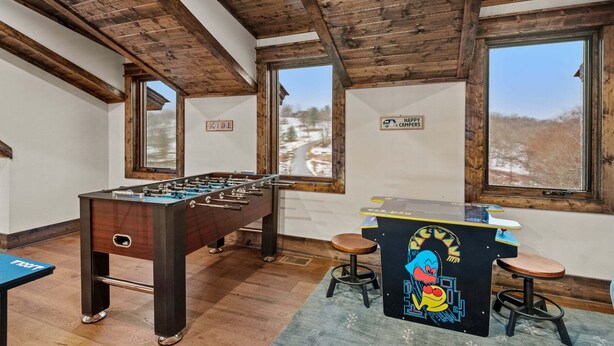 Ein Zimmer mit einem Kicker, einer Bar mit Hockern und großen Fenstern mit Blick auf eine verschneite Landschaft.