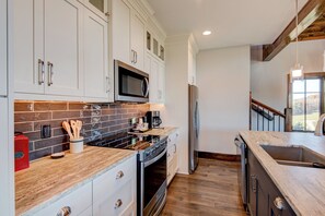 Una cocina moderna con gabinetes blancos, salpicadero de baldosas negras, electrodomésticos de acero inoxidable y suelo de madera.