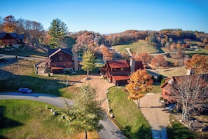 Um edifício rústico em estilo cabana, com chaminé de pedra, rodeado por um gramado bem cuidado e árvores com folhagem de outono.