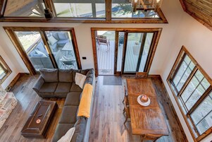 Un loft espacioso con una gran mesa de madera para comer, una zona de estar acogedora con sofá y sillones, y ventanas amplias que ofrecen vistas al exterior.