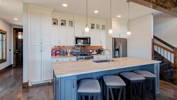 Una cocina moderna con armarios blancos, una isla grande con taburetes de bar, electrodomésticos de acero inoxidable y techo de madera.