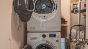 A laundry room with two stacked front-loading washing machines, a blue water heater, and a metal rack with items on it. - 7045 Brent Ln (Salt Lake City)