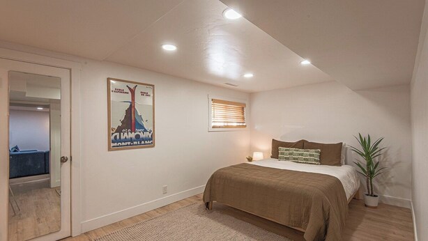 A bedroom with a bed, a potted plant, a poster on the wall, and a door leading to another room. - 7045 Brent Ln (Salt Lake City)
