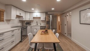 A modern kitchen with white cabinets, stainless steel appliances, and a wooden dining table. - 7045 Brent Ln (Salt Lake City)