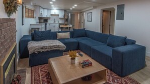 A living room with a blue sectional sofa, a wooden coffee table, and a kitchen in the background. - 7045 Brent Ln (Salt Lake City)