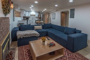A living room with a blue sectional sofa, a wooden coffee table, and a kitchen in the background. - 7045 Brent Ln (Salt Lake City)