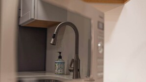 A modern kitchen with a stainless steel faucet, a small bottle of dish soap, and a white cabinet. - 7045 Brent Ln (Salt Lake City)