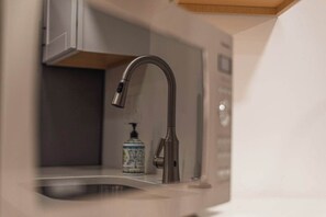 A modern kitchen with a stainless steel faucet, a small bottle of dish soap, and a white cabinet. - 7045 Brent Ln (Salt Lake City)