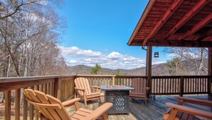 Eine Holzterrasse mit Adirondack-Stühlen und einem Tisch, mit Blick auf eine gebirgige Landschaft.