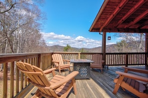 Eine Holzterrasse mit Adirondack-Stühlen und einem Tisch, mit Blick auf eine gebirgige Landschaft.