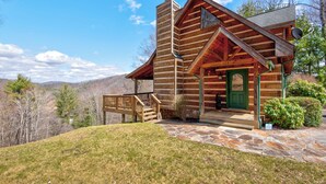 Eine Blockhütte mit einer terrasse aus Steinplatten, einer grünen Tür und einer Holztreppe zum Eingang.