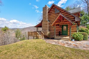 Eine Blockhütte mit einer terrasse aus Steinplatten, einer grünen Tür und einer Holztreppe zum Eingang.