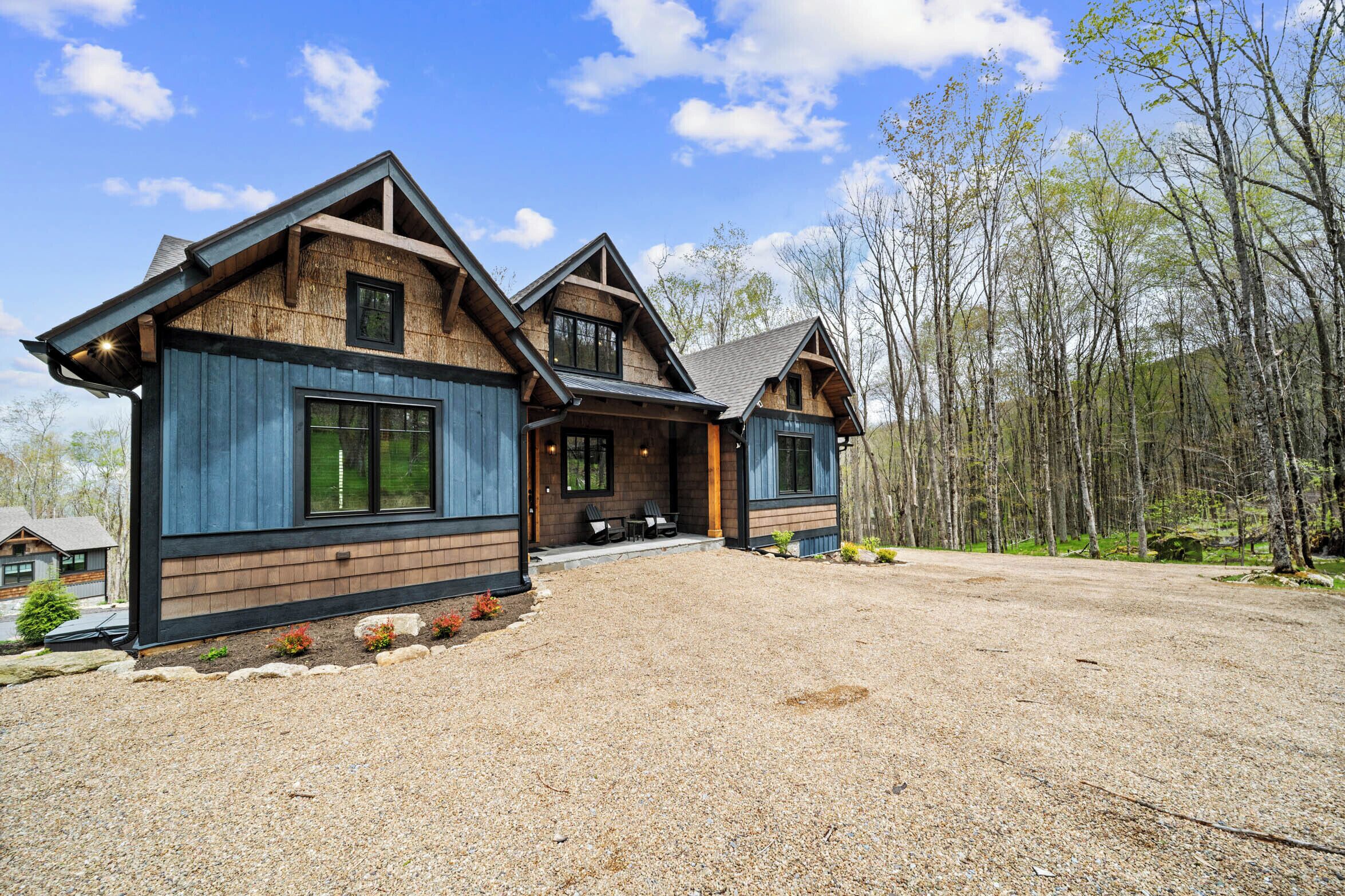 A modern log cabin with a gravel driveway and a forest backdrop.