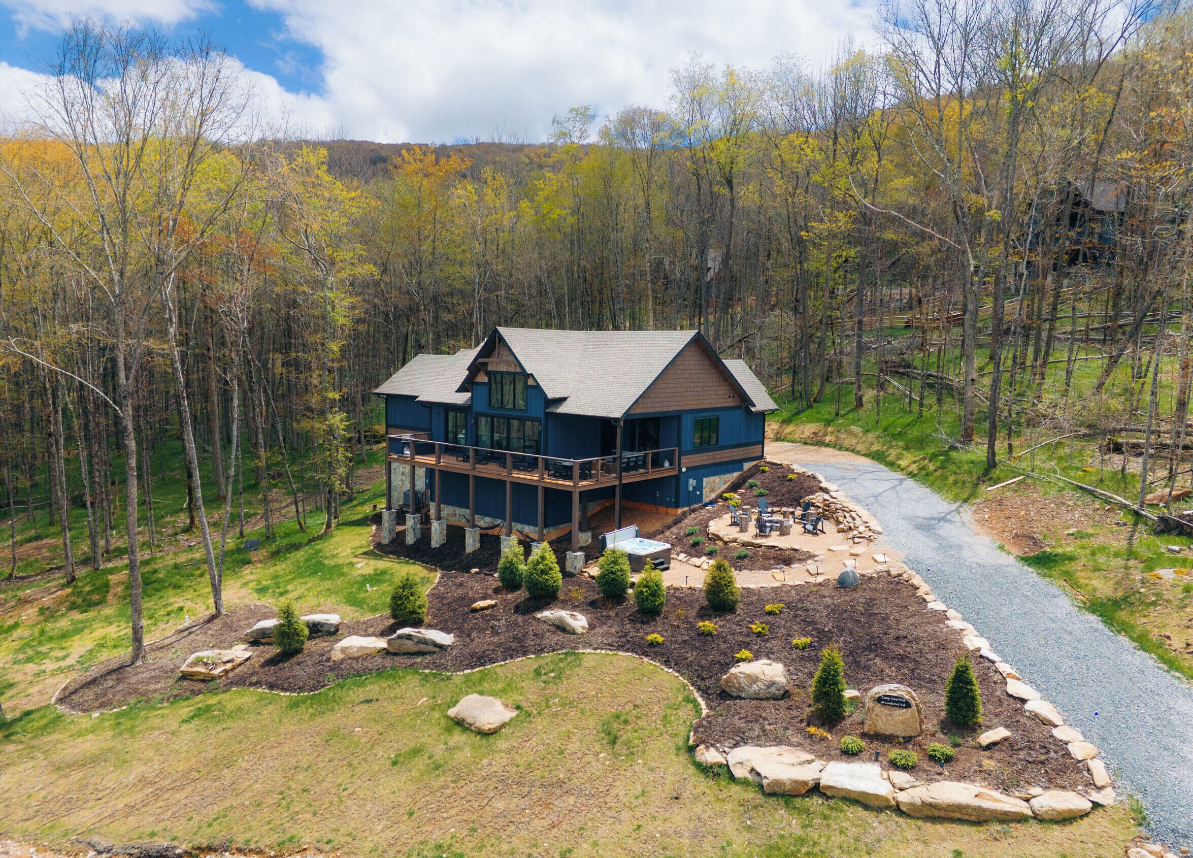 A large, two-story house with a deck, surrounded by a forested area.