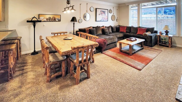 Amplia sala de estar con una mesa de comedor de madera, un sofá y una mesa de centro. Se observan varias decoraciones en las paredes, incluyendo cuadros y espejos.