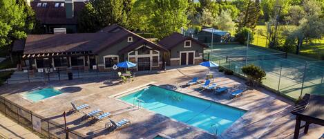 A pool area with two pools, lounge chairs, umbrellas, and a view of mountains.