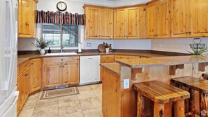 Una cocina con armarios de madera, lavavajillas, ventana con persianas y un reloj en la pared.