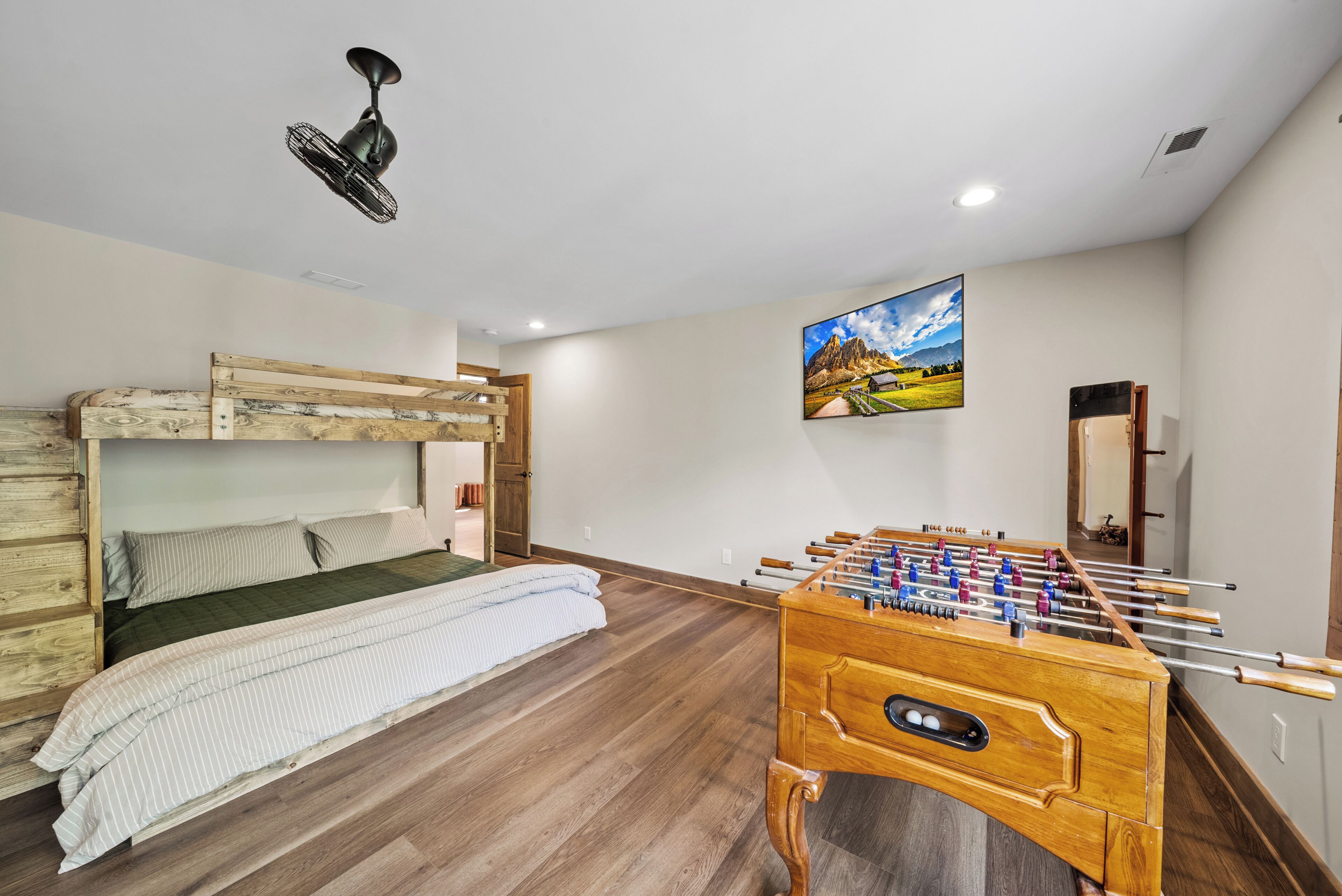 Una habitación con una cama litera, una mesa de fútbol de mesa, un cuadro en la pared y un ventilador de techo.