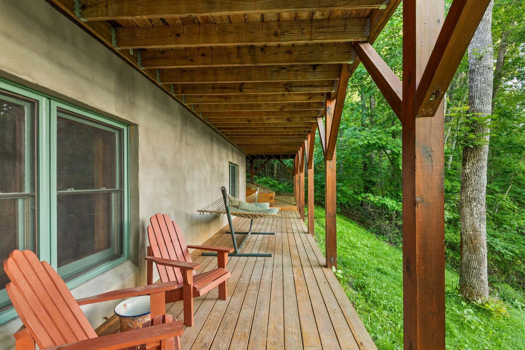 A wooden deck with Adirondack chairs and a hammock, surrounded by lush greenery.