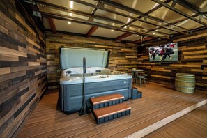 A hot tub in a rustic room with wooden walls, a television, and a barrel. - Matney Ridge Estate (Banner Elk)