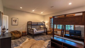 A bedroom with a bunk bed, a desk with a chair, a television, a window with blinds, and a blanket on the floor. - Matney Ridge Estate (Banner Elk)