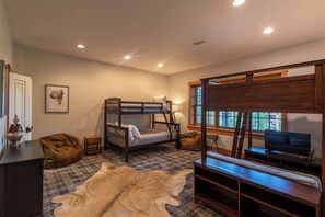 A bedroom with a bunk bed, a desk with a chair, a television, a window with blinds, and a blanket on the floor. - Matney Ridge Estate (Banner Elk)