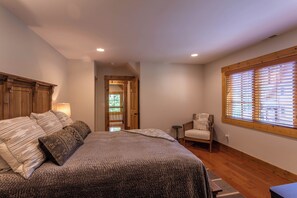 A bedroom with a large bed, a chair, a window with blinds, and a door leading to another room. - Matney Ridge Estate (Banner Elk)