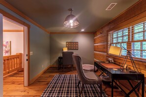 A cozy room with a wooden floor, a checkered rug, a desk with a lamp, a chair, and a window with blinds. - Matney Ridge Estate (Banner Elk)