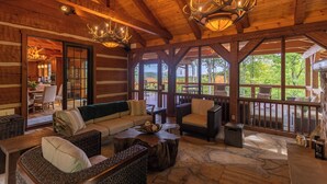 A log cabin interior with a wooden ceiling, chandeliers, a stone floor, and a view of the outdoors. - Matney Ridge Estate (Banner Elk)