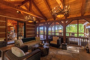 A log cabin interior with a wooden ceiling, chandeliers, a stone floor, and a view of the outdoors. - Matney Ridge Estate (Banner Elk)