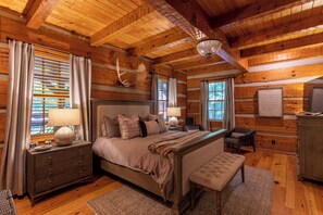 A log cabin bedroom with a large bed, a bench, a dresser, and a chandelier. - Matney Ridge Estate (Banner Elk)