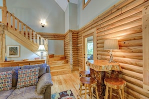 A log cabin interior with a staircase, a sofa with patterned cushions, a table with a lamp, and a rustic wooden chair. - Hideaway Homestead (Banner Elk)