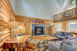 A log cabin interior with a fireplace, wooden furniture, and a balcony. - Hideaway Homestead (Banner Elk)